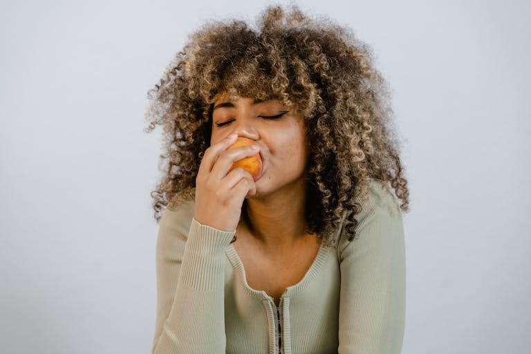 Woman Wearing Long Sleeve Shirt Eating a Fruit
