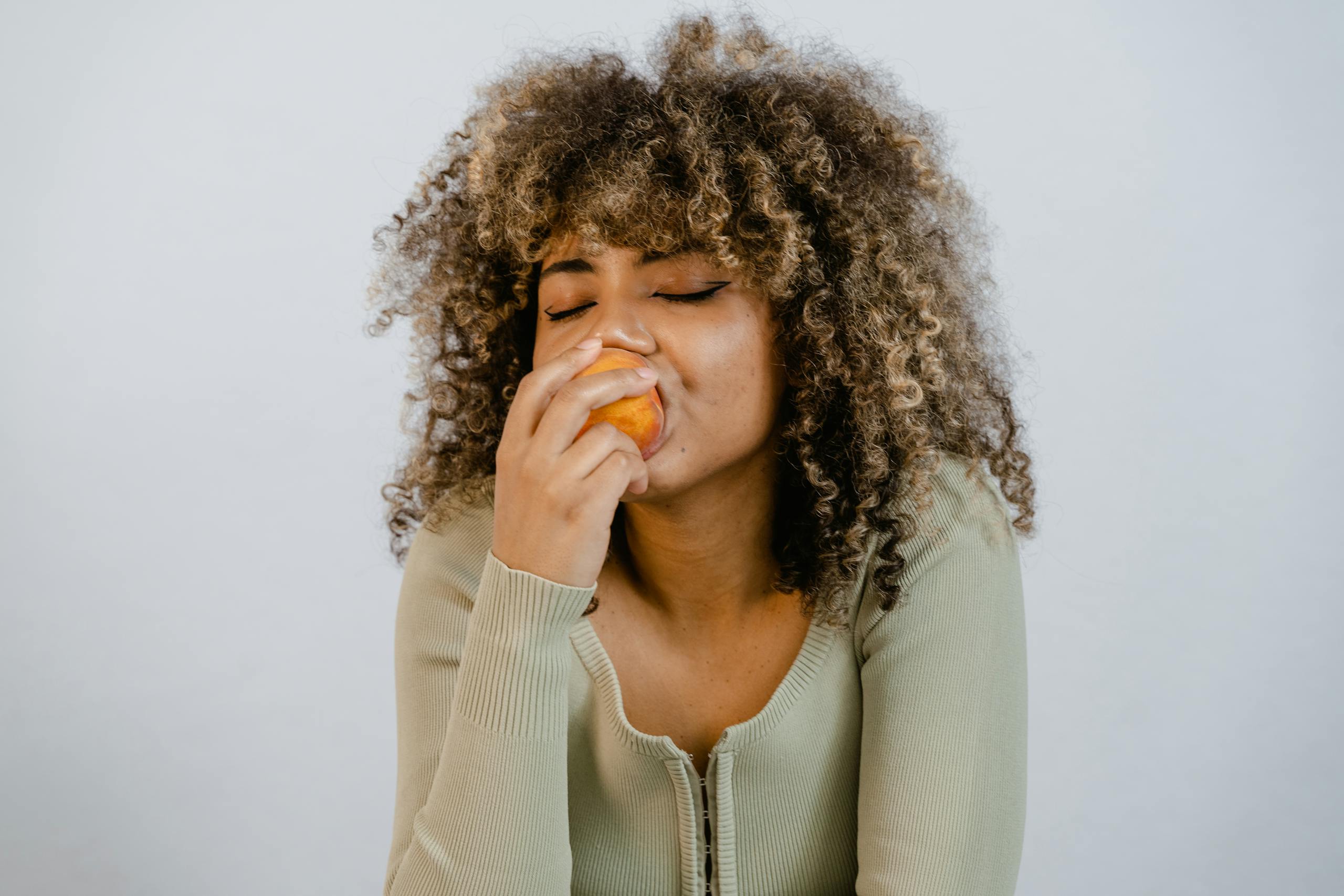 Woman Wearing Long Sleeve Shirt Eating a Fruit
